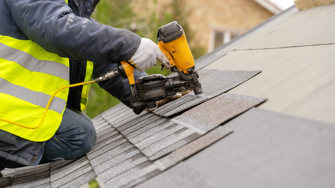 A roofer holding an electric nail gun while placing roof tiles.
