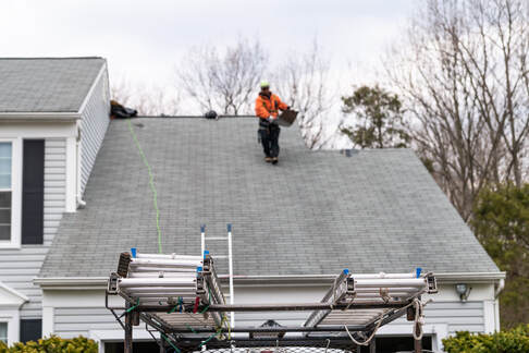 A picture of a roofer walking down with a rooftile for a roof replacement to prevent leaks.